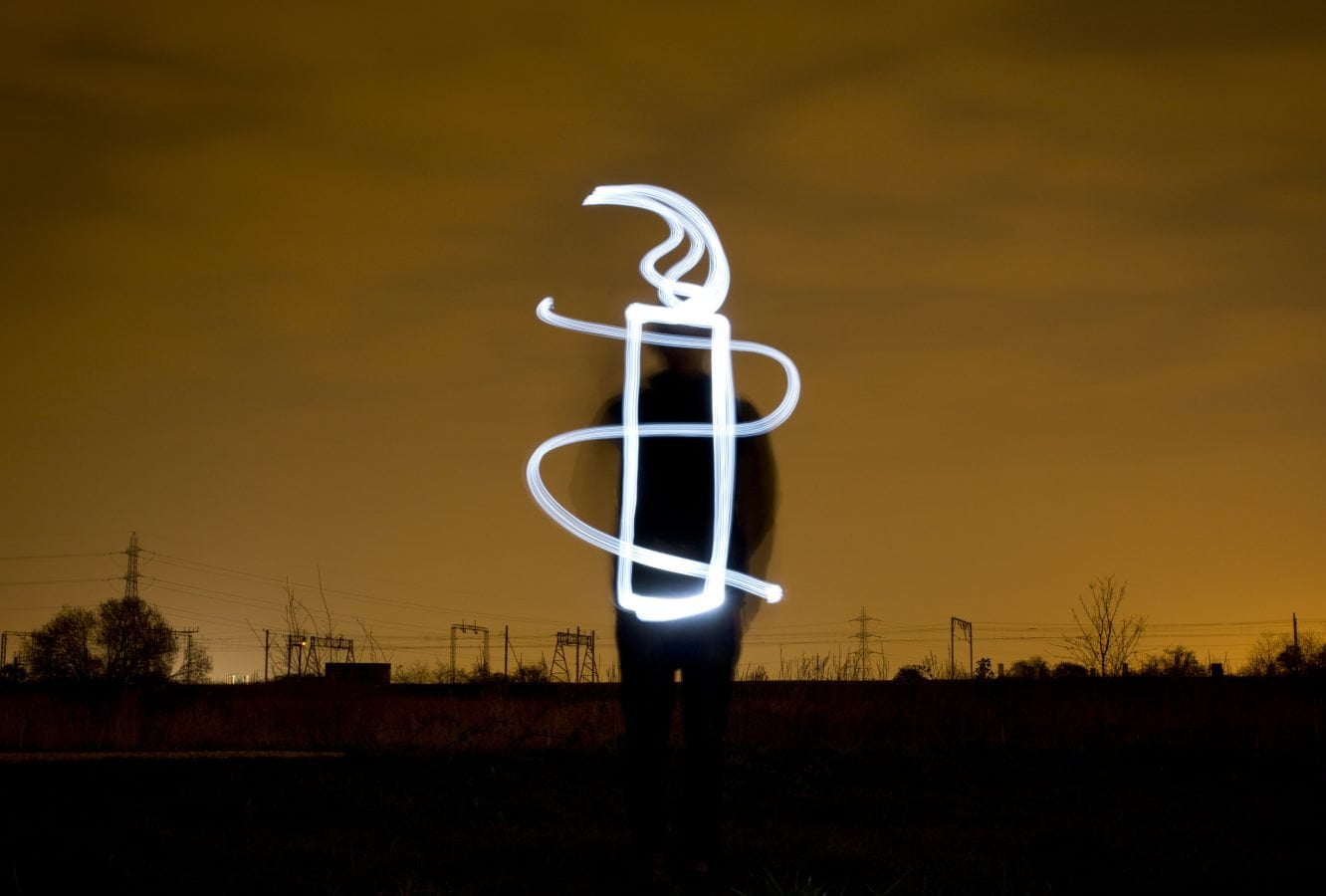 Amnesty Candle - light drawing. A light artist stands against a dark night sky and paints the AI candle.