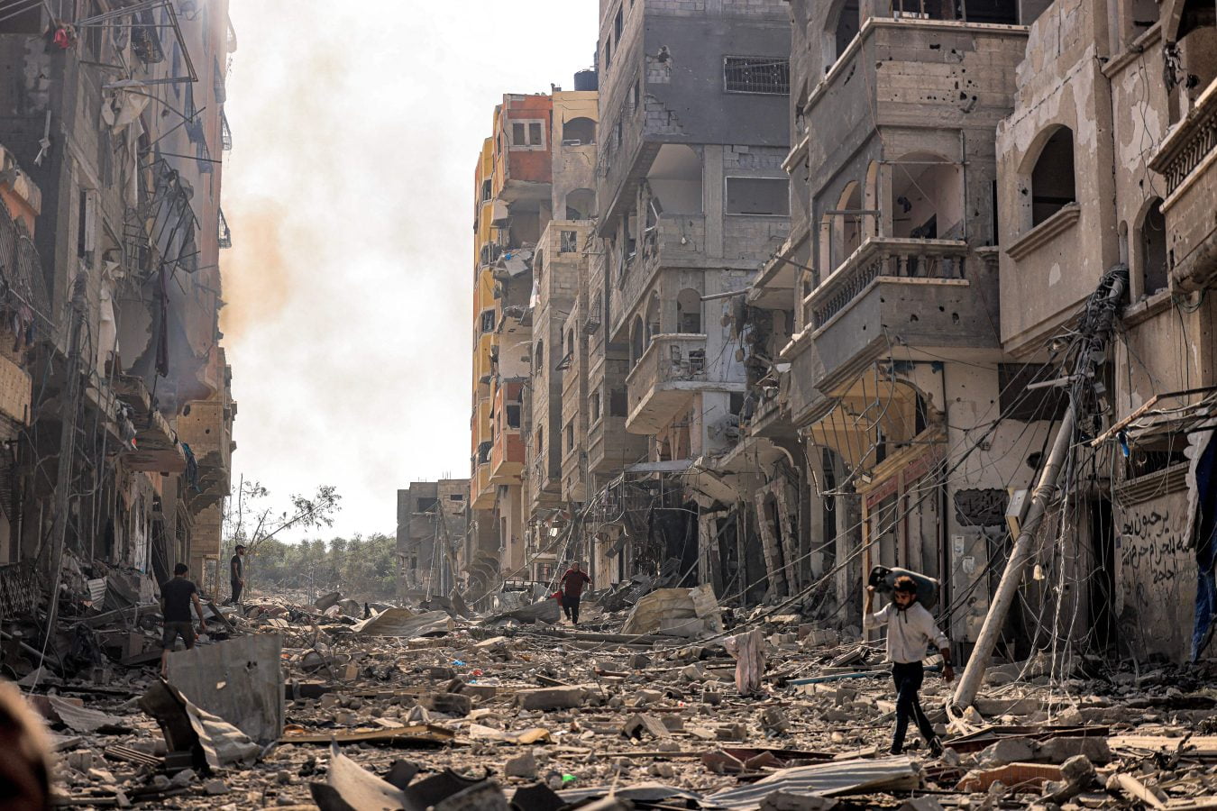 A man carries a propane gas cylinder on his back while walking through debris and destruction littering a street in the Jabalia camp for Palestinian refugees in Gaza City on October 11, 2023. (Photo by MAHMUD HAMS / AFP) (Photo by MAHMUD HAMS/AFP via Getty Images)