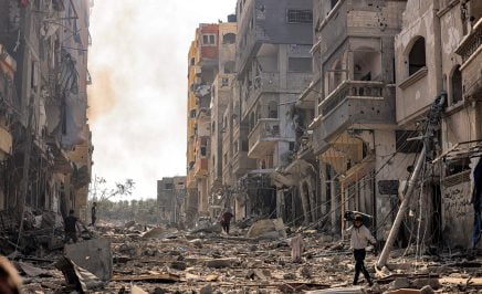 A man carries a propane gas cylinder on his back while walking through debris and destruction littering a street in the Jabalia camp for Palestinian refugees in Gaza City on October 11, 2023. (Photo by MAHMUD HAMS / AFP) (Photo by MAHMUD HAMS/AFP via Getty Images)