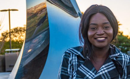 a young woman with dark skin, smiling, as the sun sets behind her